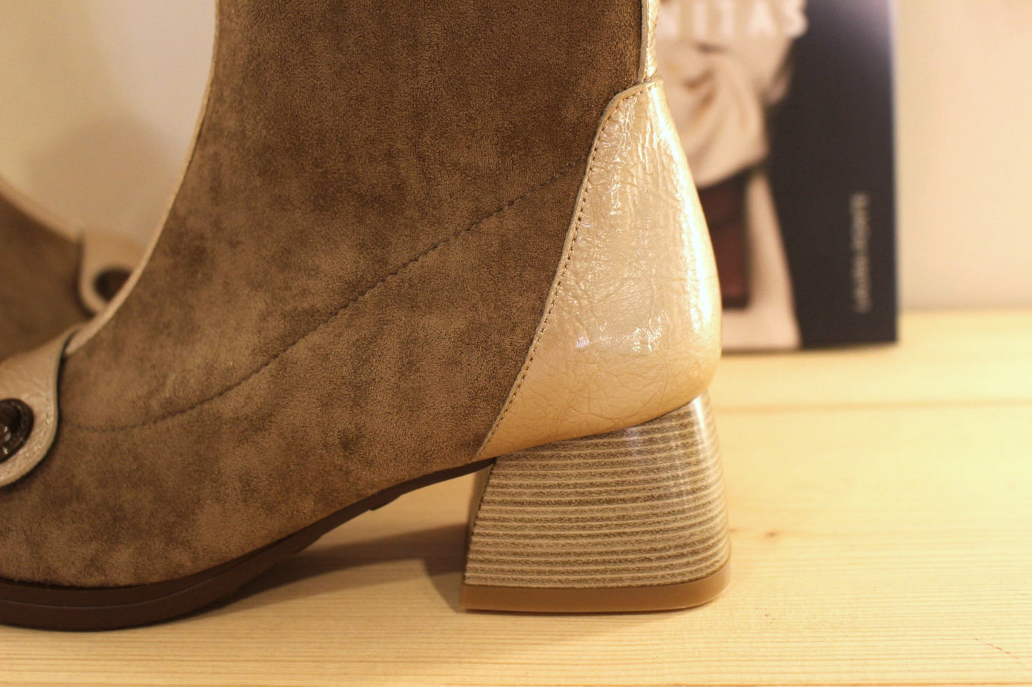 Bottine en cuir lisse de couleur crème avec une patine légèrement bruni. Bride vernis crème et bouton étain sur le coup de pied. Tige en velours taupe avec arrière vernis.