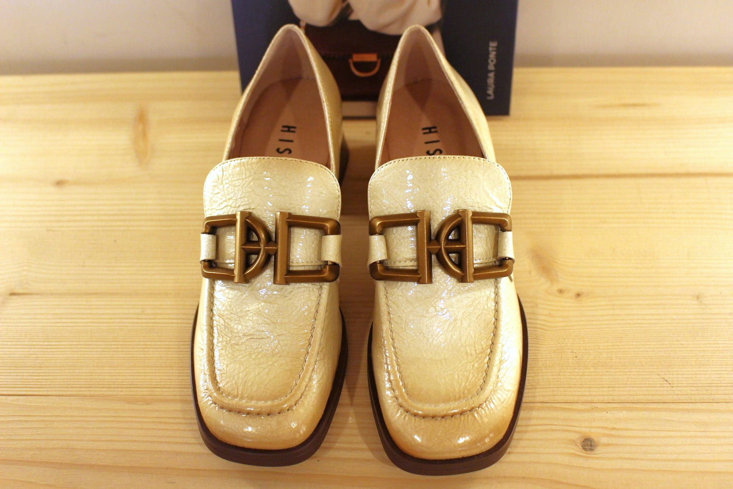 Mocassins en cuir vieillit, vernis de couleur crème avec une patine légèrement bruni. Boucle déco sur le coup de pied.