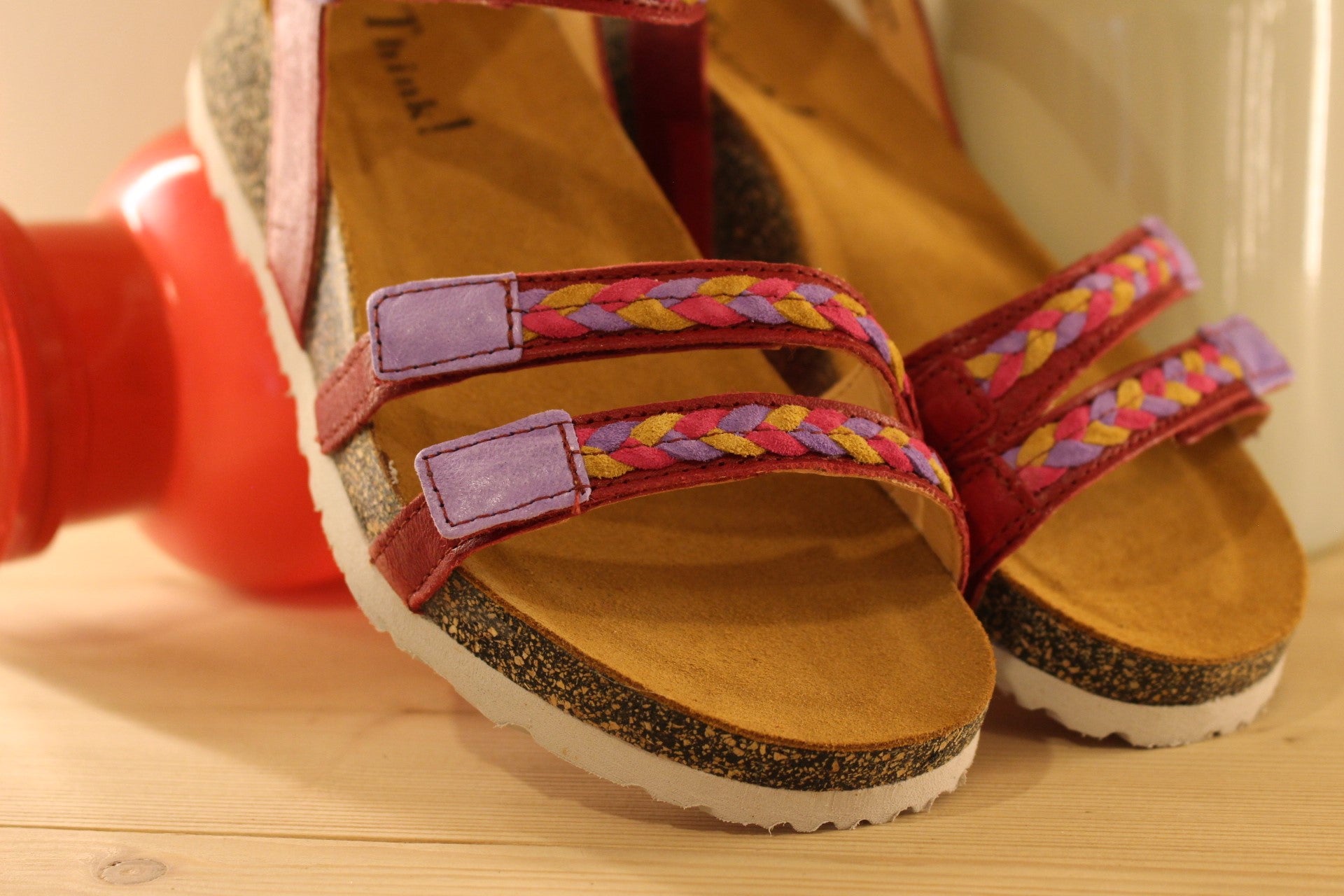 Sandales THINK en cuir de couleur rouge fraise. Habillage des brides en tressé de cuirs colorés parme, rouge et jaune. Serrage par trois scratchs. Chaussures extra légères. Semelle interne anatomique