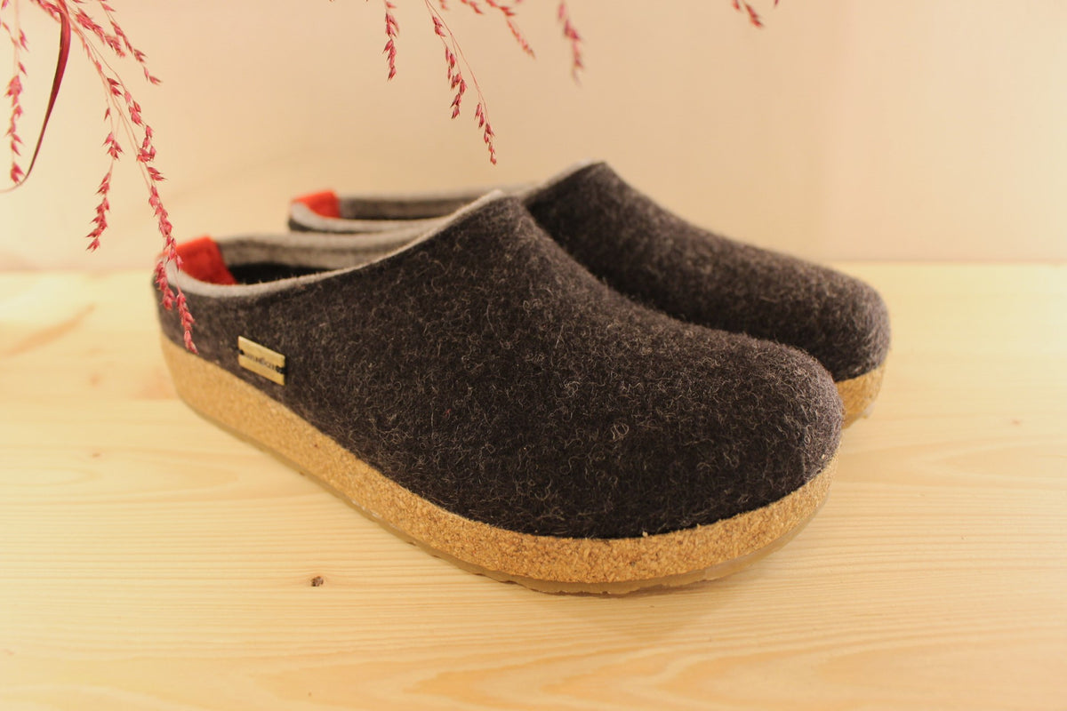 Chaussons HAFLINGER coupe sabot en pure laine de couleur graphit avec un double contour de coup de pied de couleur gris clair. Retour à l'arrière assez montant pour permettre un meilleur maintien à la marche
