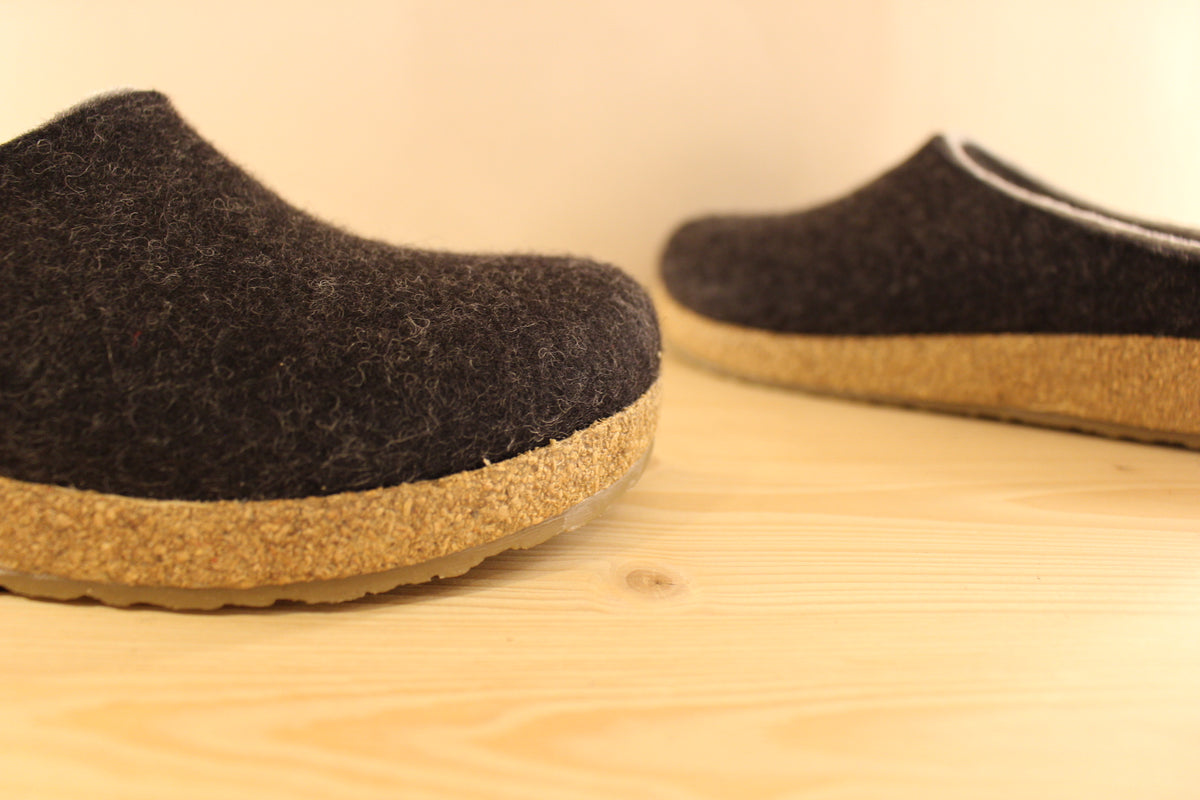 Chaussons HAFLINGER coupe sabot en pure laine de couleur graphit avec un double contour de coup de pied de couleur gris clair. Retour à l'arrière assez montant pour permettre un meilleur maintien à la marche