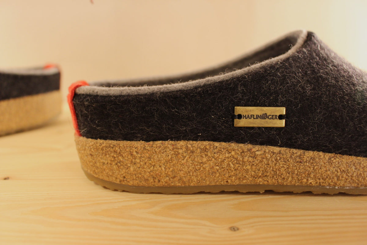 Chaussons HAFLINGER coupe sabot en pure laine de couleur graphit avec un double contour de coup de pied de couleur gris clair. Retour à l'arrière assez montant pour permettre un meilleur maintien à la marche