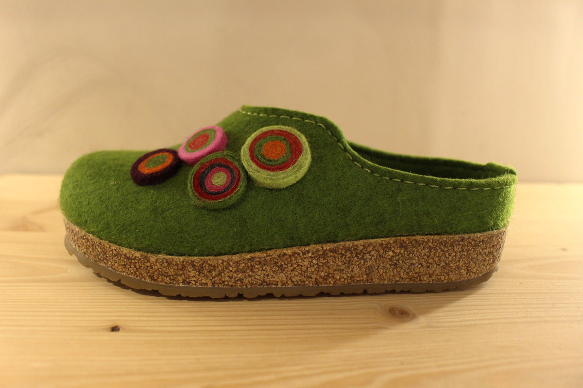  Chaussons HAFLINGER coupe sabot en pure laine de couleur vert ou beige. Déco de boutons colorés en laine sur le côté du coup de pied. Découpe asymétrique pour un bon maintien. 