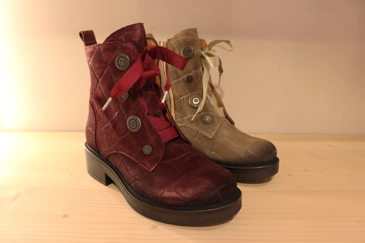 Bottines Casta en cuir velours ras et brossé de couleur bordeaux ou de couleur kaki. Cuir imprimé et habillage bouton décoratif.