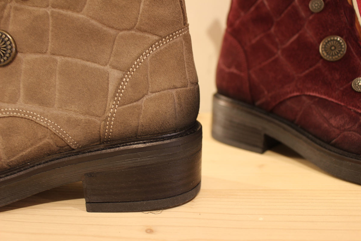 Bottines Casta en cuir velours ras et brossé de couleur bordeaux ou de couleur kaki. Cuir imprimé et habillage bouton décoratif.